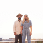 Drew and Ellie Holcomb standing together outside in promo photo for their album "Memory Bank"